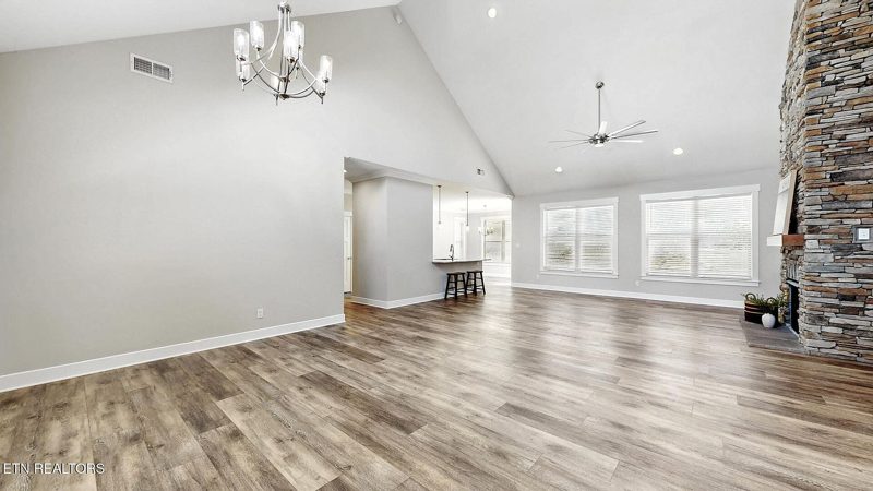 Vaulted great room with a stone fireplace and wood-look floors